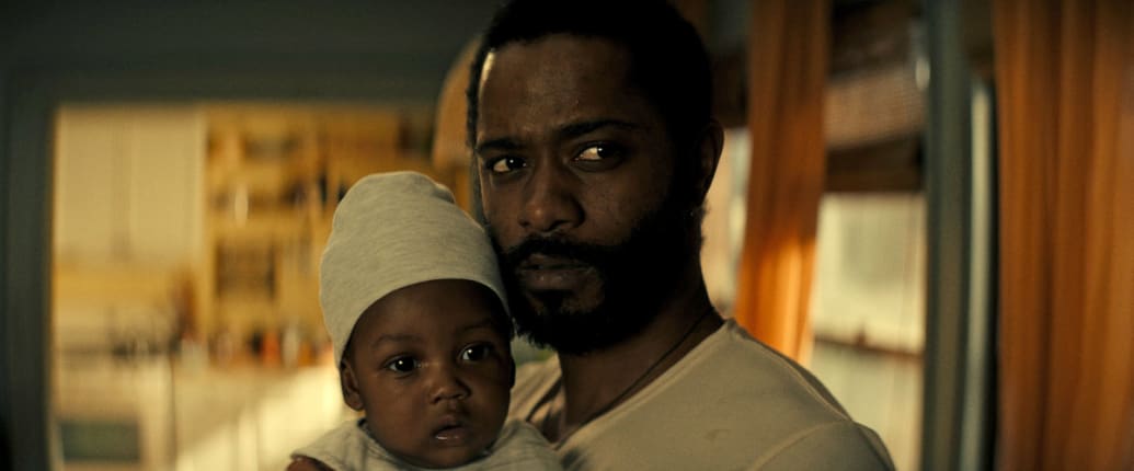 A still from ‘The Changeling’ shows LaKeith Stanfield looking into the camera and holding a baby