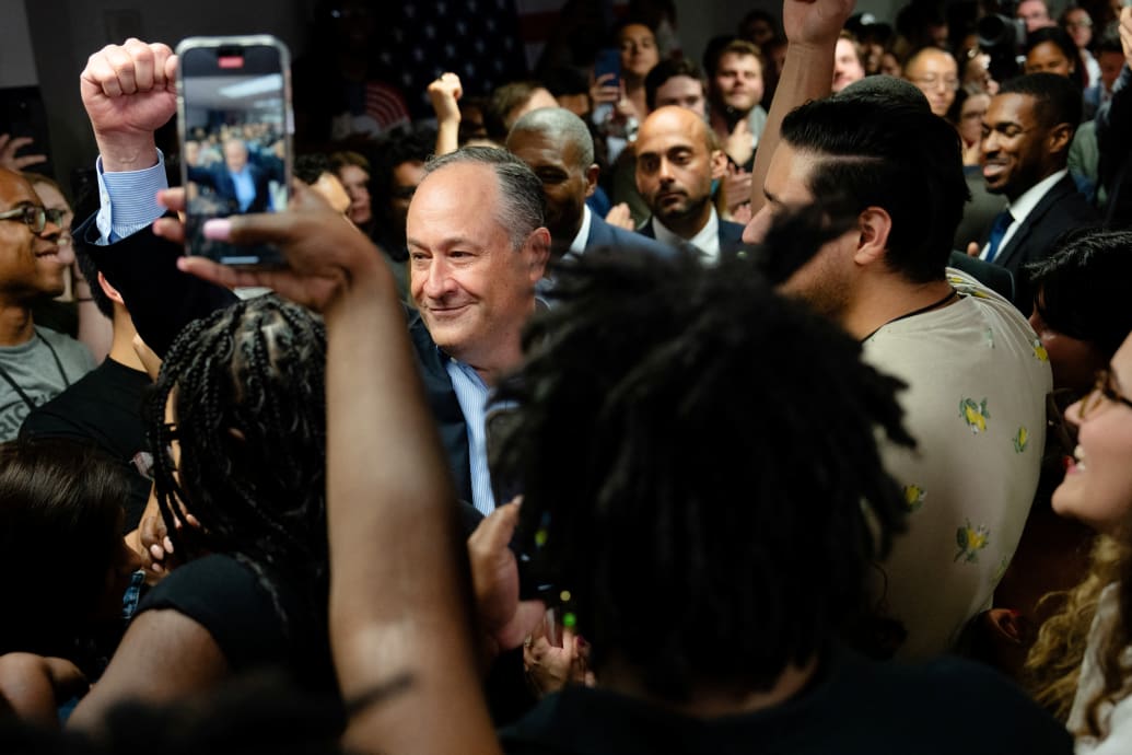 Doug Emhoff pumping his fist surrounded by people taking photos with phones