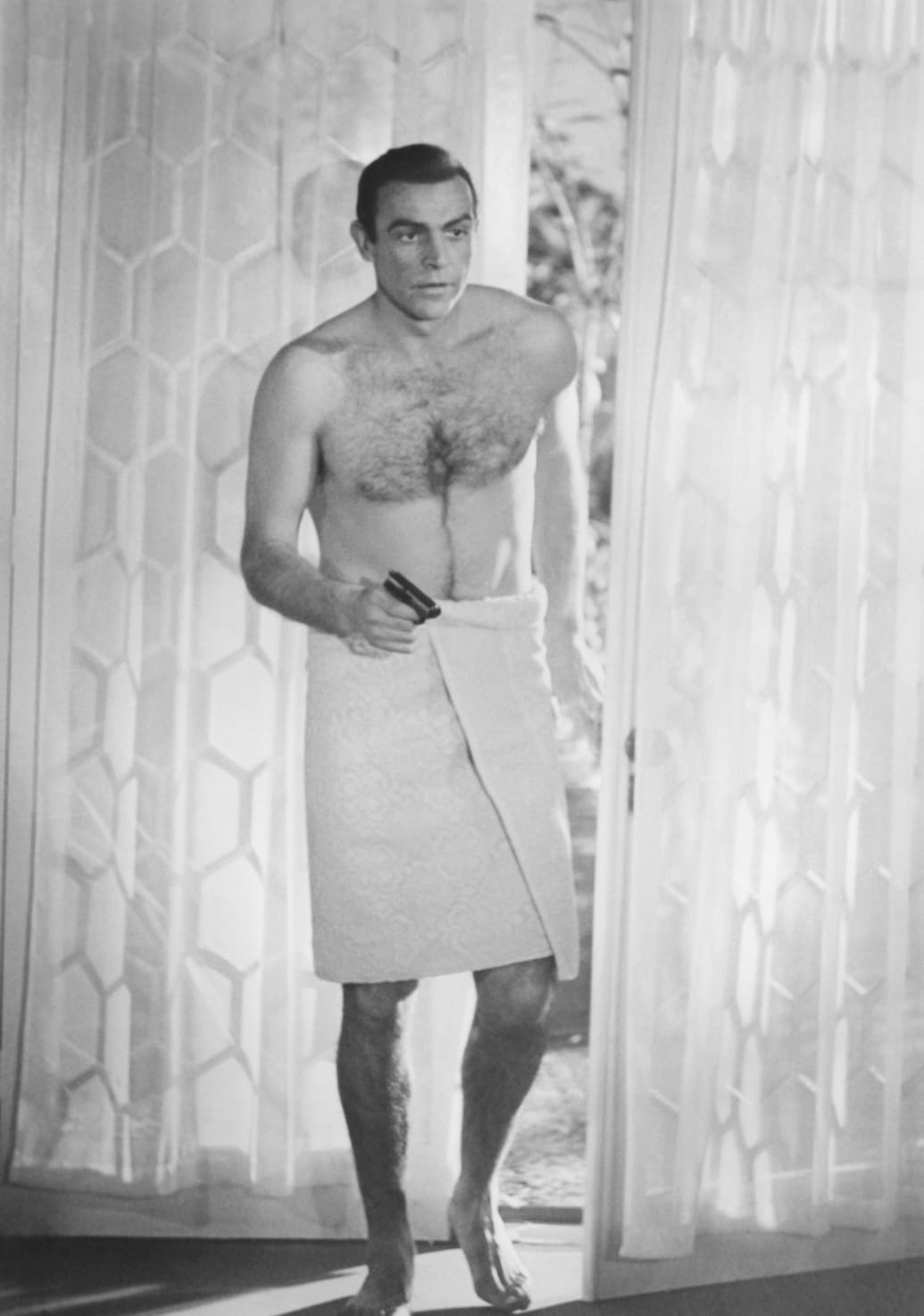 Sean Connery holds gun bare-chested with a towel around his waist as James Bond in the 1963 film From Russia With Love