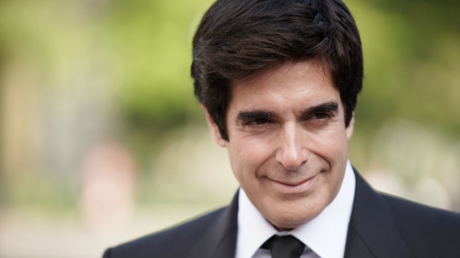 David Copperfield, wearing a suite and tie, stares to his left outdoors.