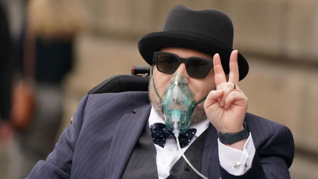 Nicholas Rossi throws up a peace sign as he is wheeled out of court in 2022.