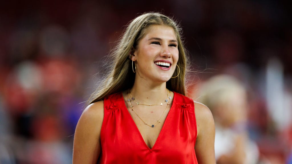 Ava Hunt smiles while walking on an NFL field in a red top.