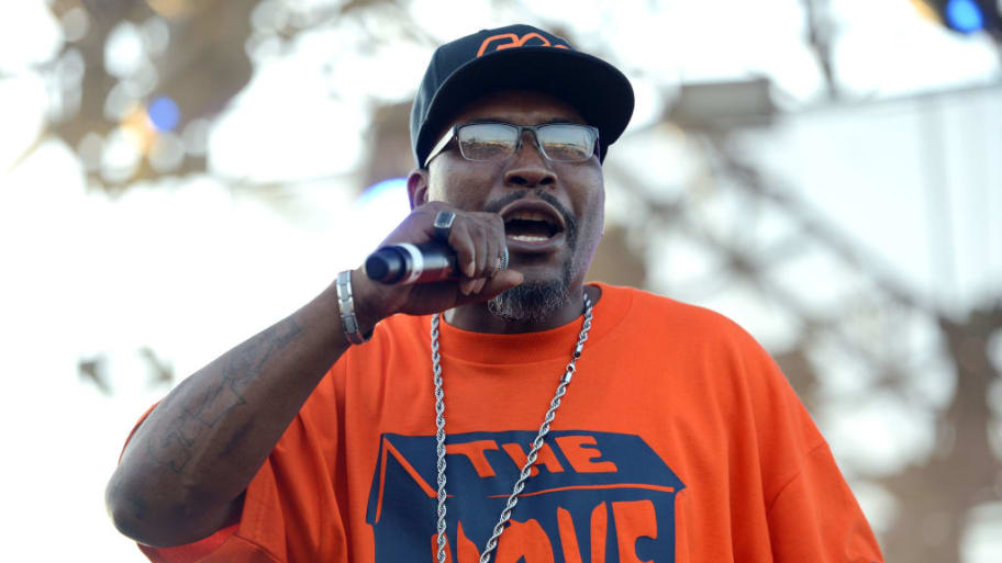 C-Knight, wearing an orange shirt and holding a microphone, performs on stage.