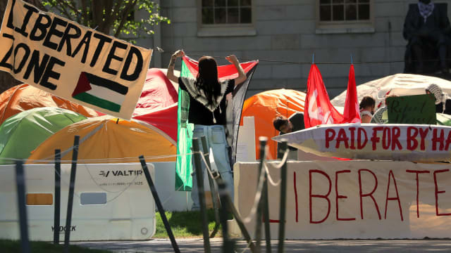 A protester hangs a Palestinian flag at an encampment on Harvard Yard.