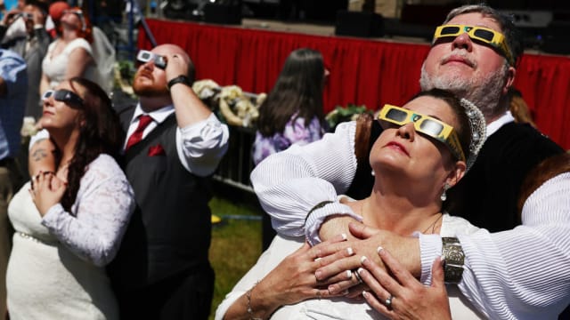 Two brides and grooms look up at the solar eclipse from an Arkansas field.