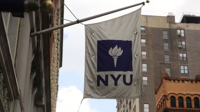 A white and purple NYU banner hangs from a building in New York City.