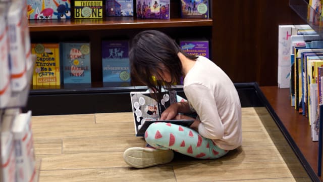 A young girl sits on the floor and reads in a bookstore.
