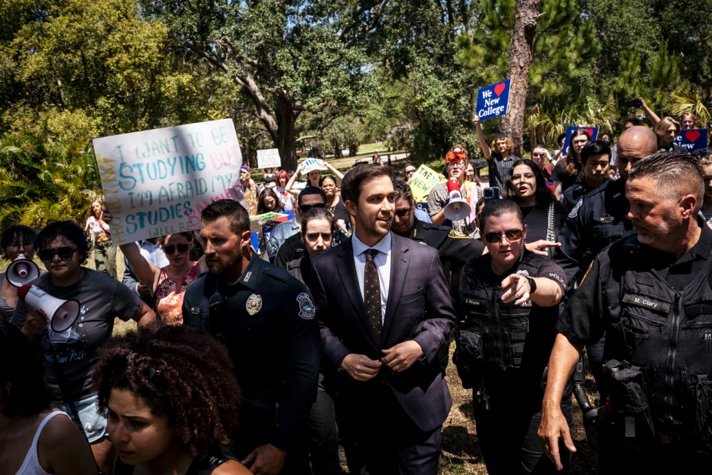 A photograph of Christopher Rufo walking through protestors on the New College campus in Florida.