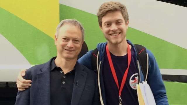 Gary Sinise, left, smiles with his son Mac, right, in front of a bus.