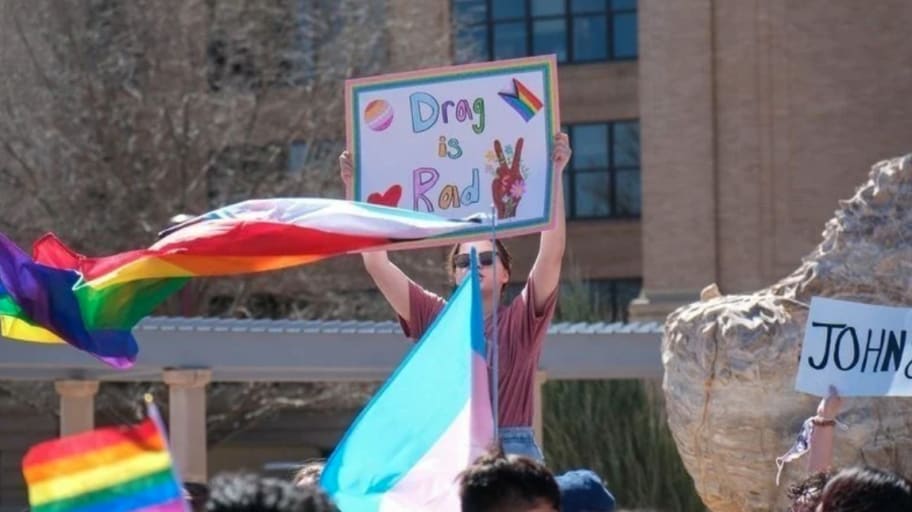 A protester holds a sign saying "Drag is rad" amid pride flags