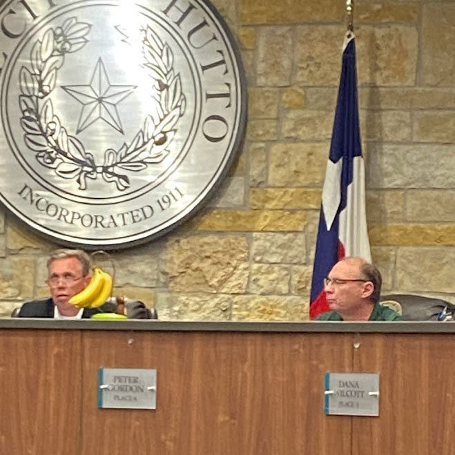 A photograph of Mayor Mike Snyder to the right and a city council member with the banana stand on top of the dais.