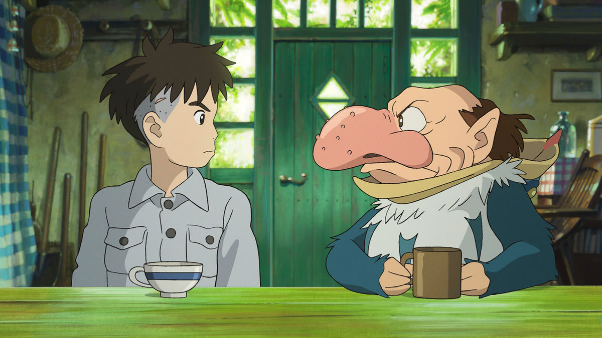 A still from ‘The Boy and the Heron,’ featuring a boy and a man in an animal outfit sitting at a table.