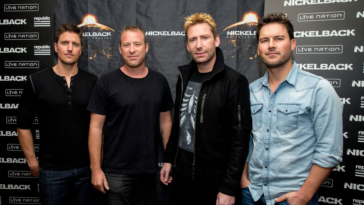 A photo of the band Nickelback standing in front of a step and repeat.