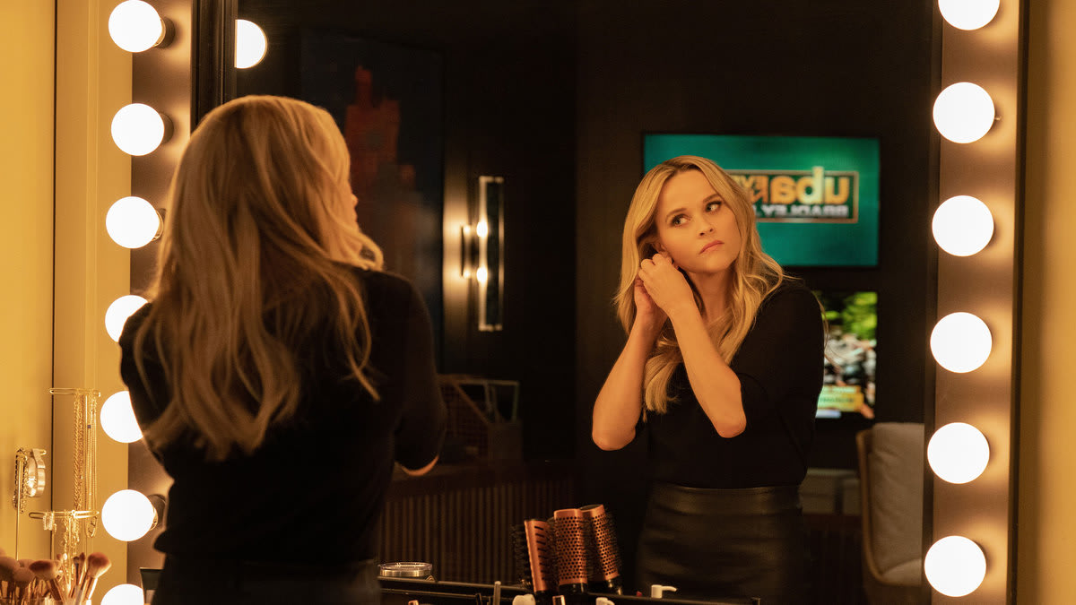 A still from ‘The Morning Show’ shows Reese Witherspoon putting on earrings in a mirror