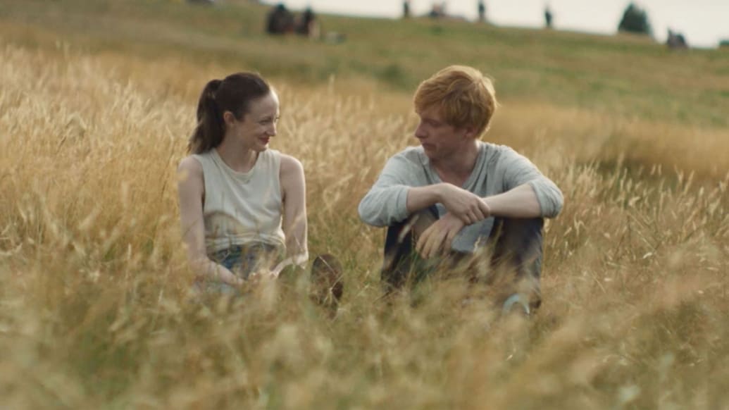 Andrea Riseborough and Domhnall Gleeson sit in a field in a still from ‘Alice & Jack’
