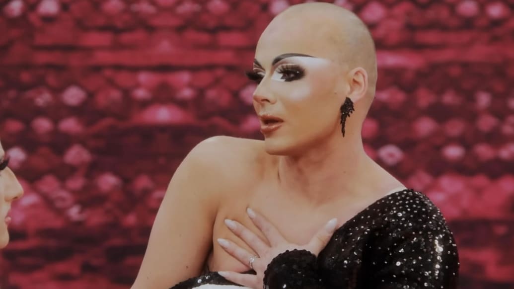 Q on a couch in a still from Ru Paul’s Drag Race