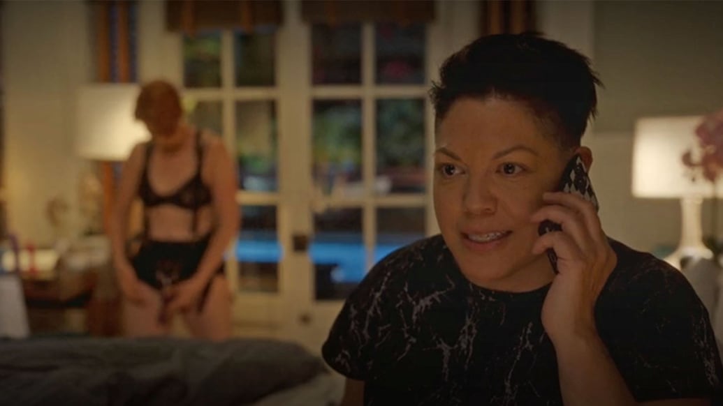 Cynthia Nixon trying on a strap on while Sara Ramirez is on the phone in a still from And Just Like That