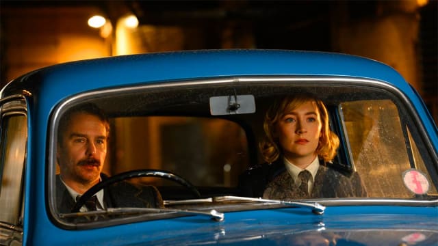 A man and woman sit in the front seat of a blue car.
