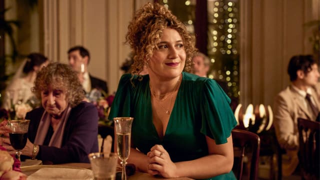 Rose Matafeo sitting at a table in a green dress at a wedding in ‘Starstruck’