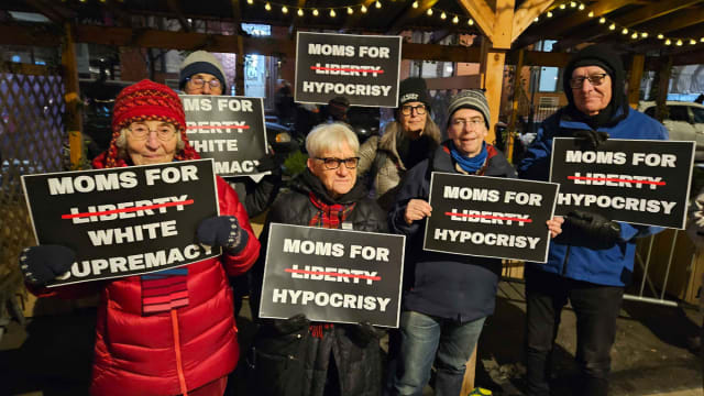 A group of protesters hold signs at a Moms for Liberty event