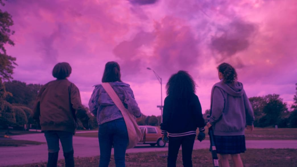 A group of four girls look up at a pink sky. 