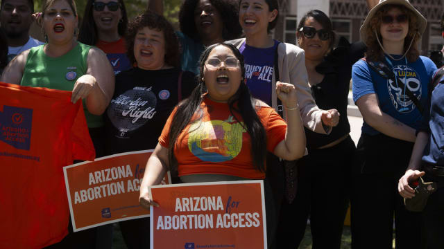 Women protest outside the Arizona legislature holding signs reading "Arizonans for Abortion Access"
