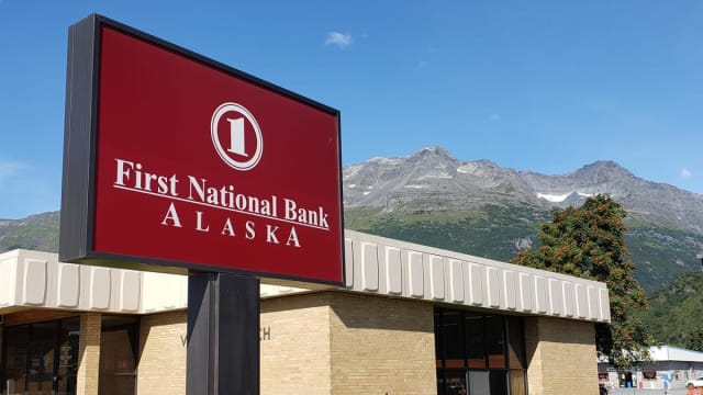 A photo of a First National Bank Alaska branch, with mountains in the distance.