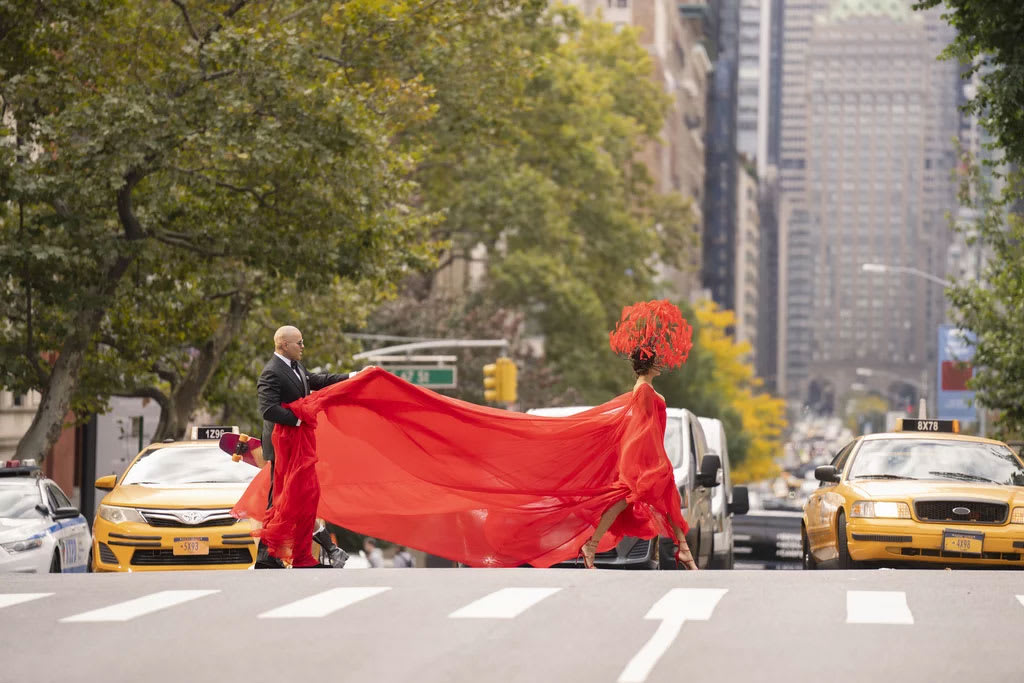 A still from And Just Like That showing Lisa Todd Wexley crossing 5th avenue in a flowing red dress.