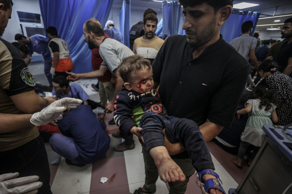 A bloodied child is carried through a busy hospital.