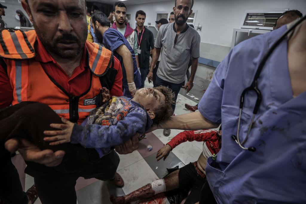 A bloodied child is carried through a busy hospital.