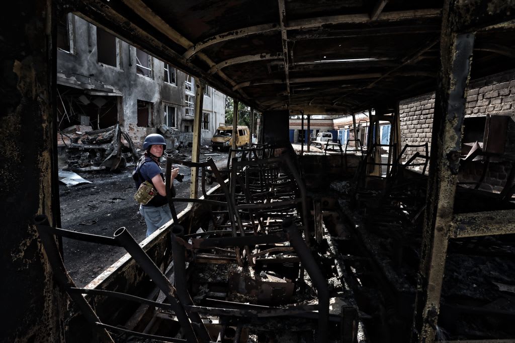 A journalist works near burnt wreckage of vehicles and a building damaged due to hostilities in Sudzha, Russia, in the Kursk Oblast.