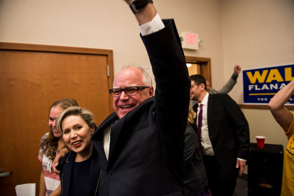 Tim Walz raises his hand while smiling with his wife.