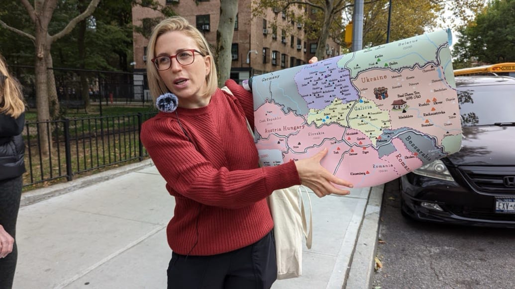A blonde woman in glasses holds a map on a sidewalk