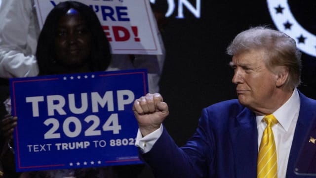 Republican presidential candidate and former U.S. President Donald Trump gestures as a supporter looks on during a Turning Point USA event.