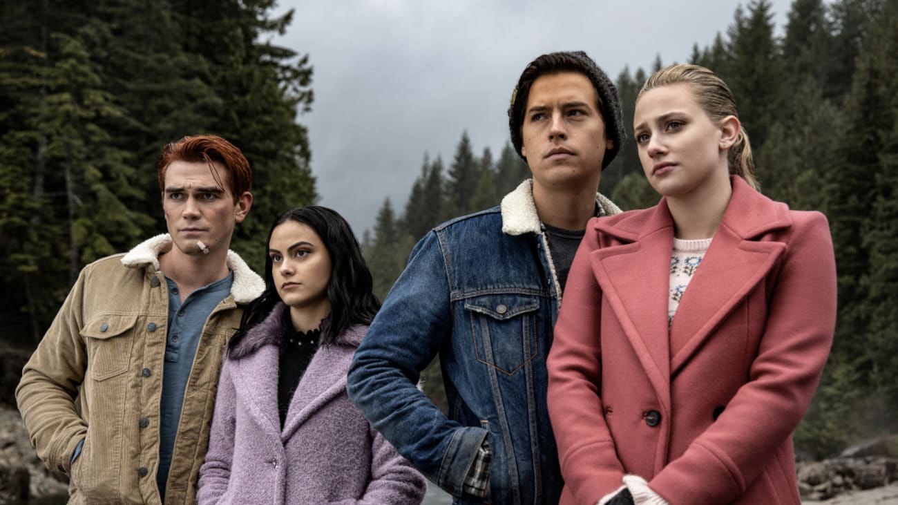 Four teenagers in coats stand together outside, looking mournful.
