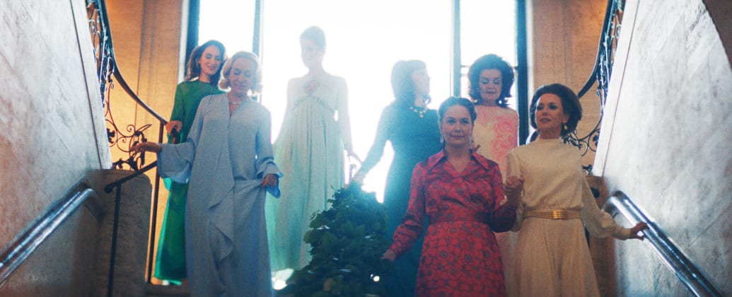 A still from FEUD: Capote Vs. The Swans episode "Ice Water in Their Veins" showing Chloe Sevigny as C.Z. Guest,  Naomi Watts as Babe Paley, Diane Lane as Slim Keith, descending stairs and dressed up glamoursly.
