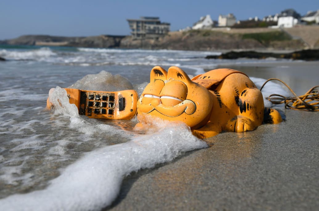 A Garfield phone sits on the beach with waves behind it.