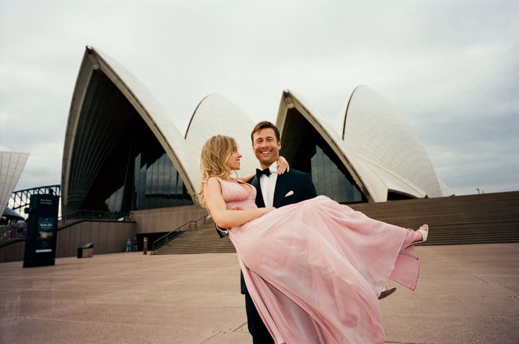 Glenn Powell carries Sydney Sweeney in front of the Sydney Opera House in a still from ‘Anyone But You’