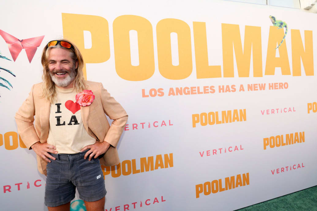 Chris Pine poses in front of a step and repeat at the premiere of Poolman