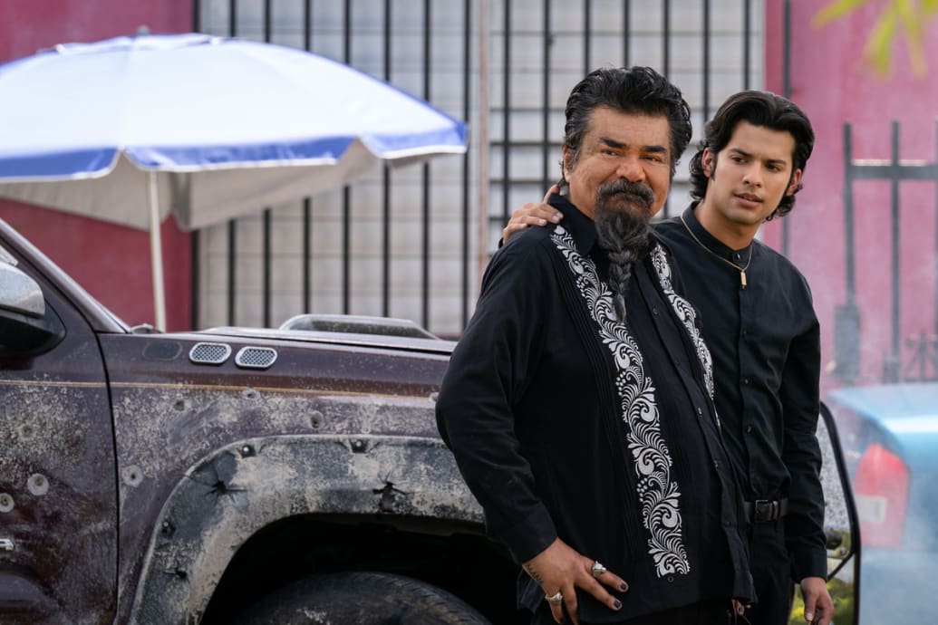 A still from ‘Blue Beetle’ shows George Lopez and Xolo Maridueña in black shirts walking down a street.