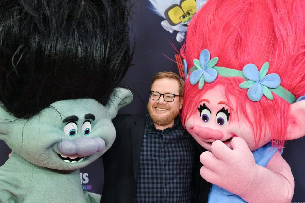 A picture of Walt Dohrn hugging two trolls on a red carpet event.