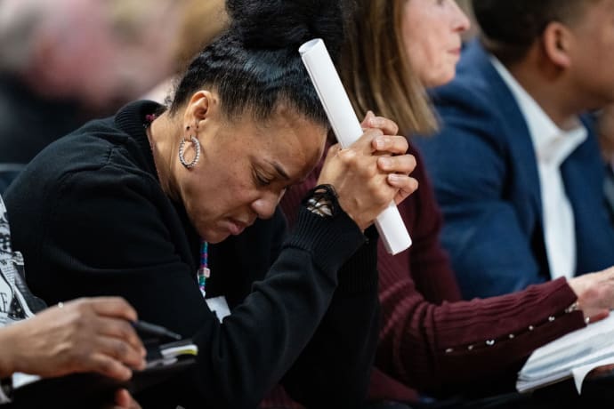 A close up of Dawn Staley sitting on the sidelines with her head in her hands.
