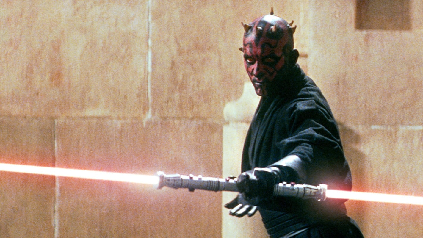 A man with a red and black face holds a lightsaber.