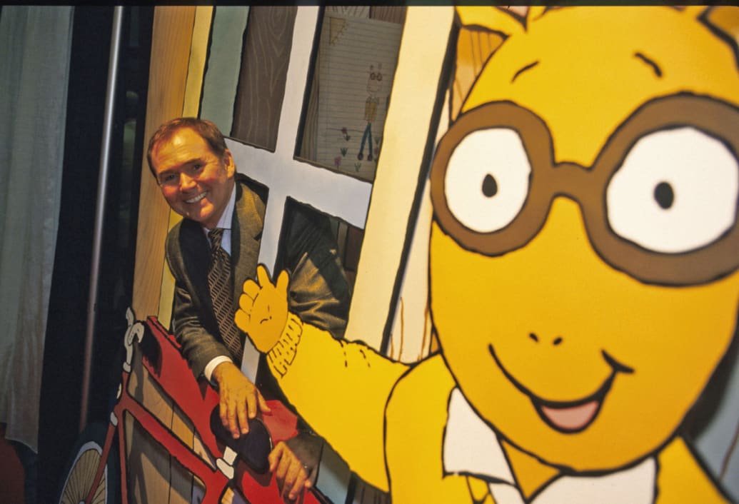 A photo of Marc Brown peeking through a window with a cutout of Arthur waving nearby.