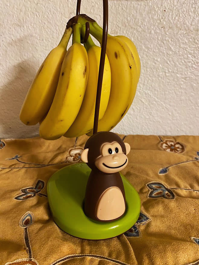 A banana holder with bananas and a monkey figurine.