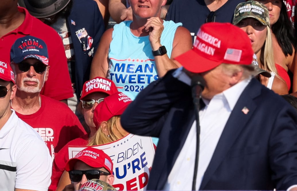 Donald Trump puts his hand to his ear after being injured in a shooting.