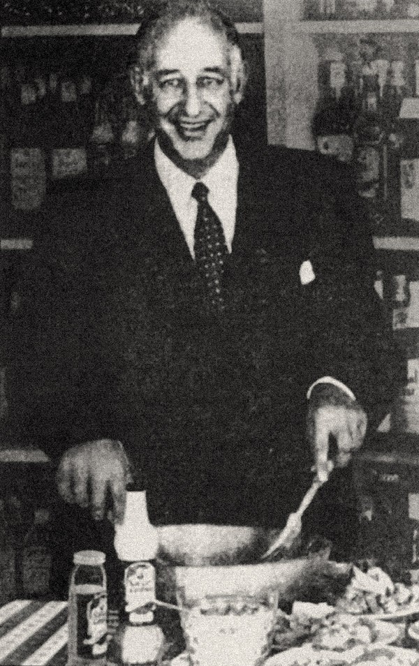 Cesare Cardini in a kitchen in front of cooking implements in black and white image