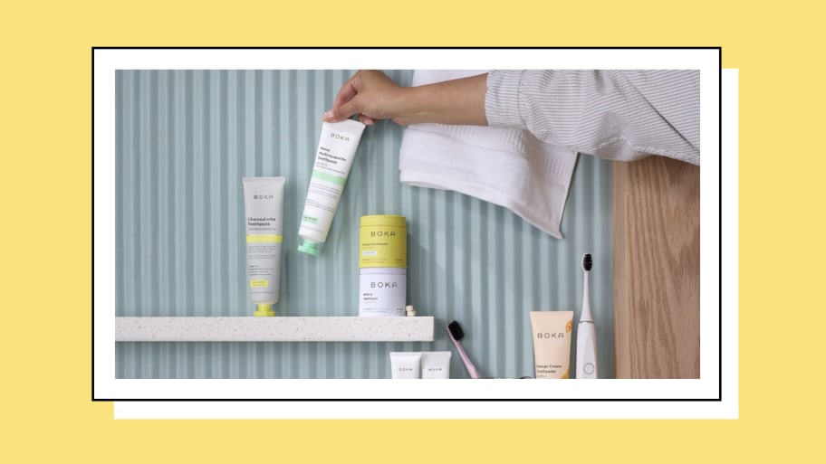 Woman placing a tube of toothpaste on a shelf next to a collection of creams, toothbrushes, and other bathroom amenities. 