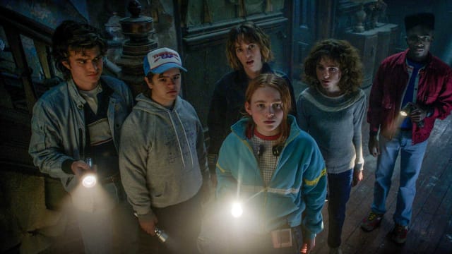 A group of teens stand around in the dark, holding flashlights.